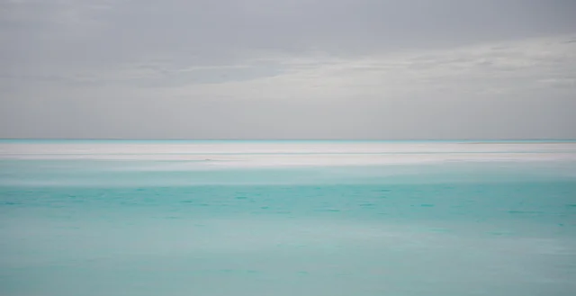 Turquoise water and white salt flats beneath a soft grey sky.