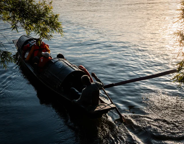 A boatman rowing a covered wooden boat through sunlit water.